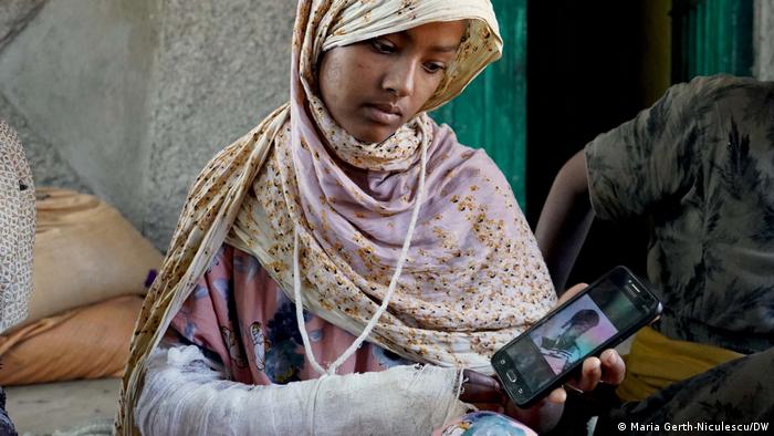 Uma jovem ferida no braço mostra uma foto no telemóvel