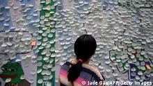 The photo taken on May 29, 2021 shows a woman looking at sticky notes containing wishes during a Pepe the Frog exhibition at a shopping mall in Beijing. - Ground down by the sapping realties of modern city life, China's youth are lying flat, the latest buzzword for those tapping out of a culture of endless work with little reward. An early icon of the burgeoning ranks of dispossessed was Pepe the Frog, also called sad frog in China, whose memes conveyed their disillusionment. - To go with AFP story China-Culture-Youth, FOCUS by Beiyi Seow (Photo by Jade GAO / AFP) / To go with AFP story China-Culture-Youth, FOCUS by Beiyi Seow (Photo by JADE GAO/AFP via Getty Images)