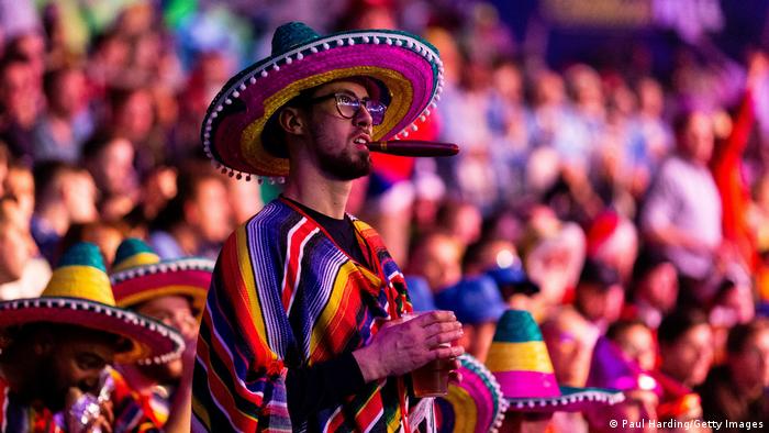 A darts fan in Mexican fancy dress watches the action