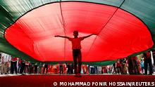 A boy poses for a picture under a massive Bangladeshi flag, during a flag rally three days ahead of the country's 50th Victory Day anniversary, in front of the parliamentary building in Dhaka, Bangladesh, December 13, 2021. REUTERS/Mohammad Ponir Hossain