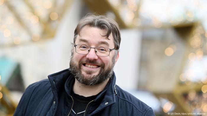 Rene Reichelt, a man with a full beard and glasses, smiling against a background of gold Christmas decorations