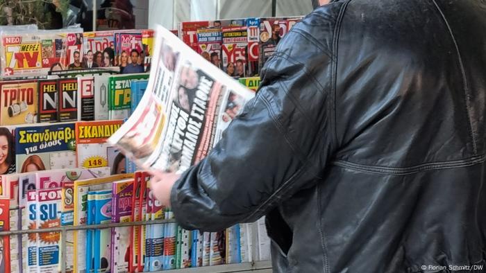 Ein Mann steht vor einem Zeitungskiosk in Griechenland und blättert in einer Zeitung