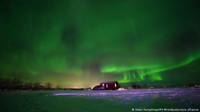 The northern lights glowing green in Iceland above a small house 