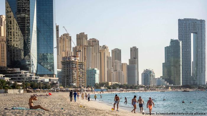 People on a sandy beach in Marina Bay in front of the Dubai skyline in the United Arab Emirates (UAE)