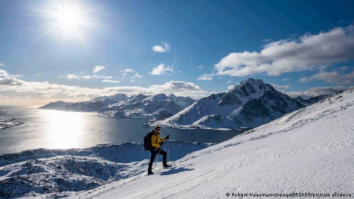 A woman on skis in front of a fjord and snow-covered mountains in Lofoten, Norway.