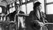 Rosa Parks sentada num assento de ônibus, com um homem branco atrás Rosa Parks sentada num assento de ônibus, com um homem branco atrás