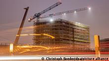 Baukräne sind an einer Baustelle in Berlin-Mitte zu sehen, wobei der Straßenverkehr sich im Vordergrund als Leuchtspuren abzeichnet. (Aufnahme mit Langzeitbelichtung und Fokusverschiebung) (zu dpa «Konjunkturprognose der Deutschen Bundesbank»)