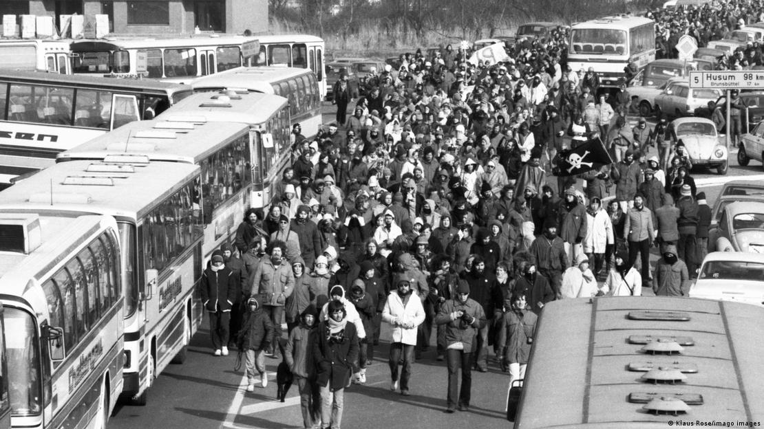 Foto preto e branca mostra muitas pessoas se deslocando ao lado de ônibus estacionados. 