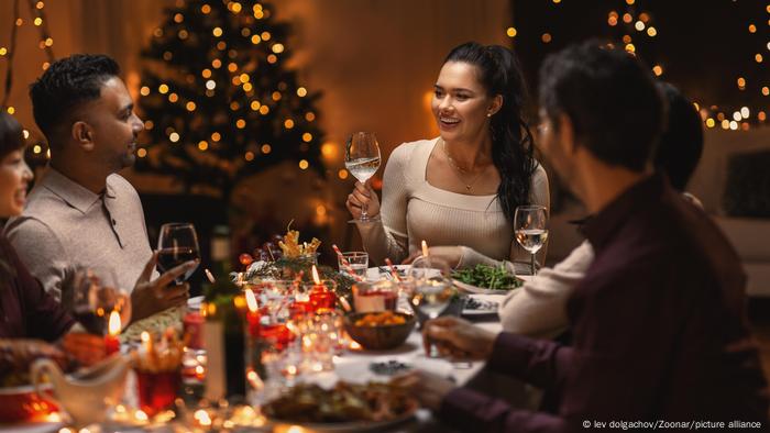 Menschen sitzen in einem weihnachtlich geschmückten Raum an einer Weihnachtstafel und prosten sich zu