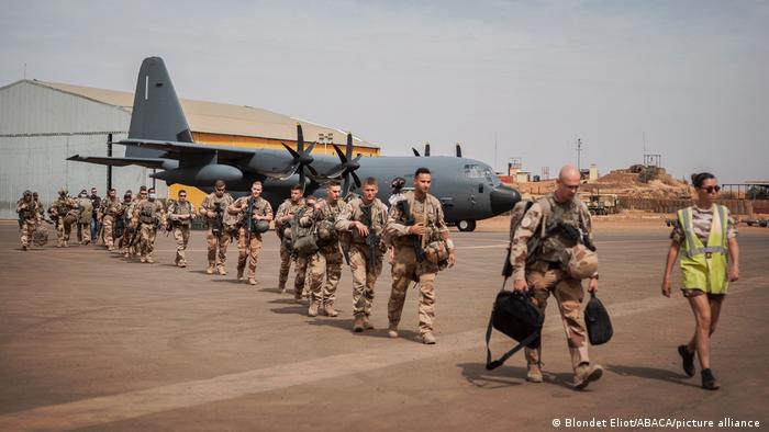 Soldaten gehen vor einem Flugzeug über einen Flugplatz