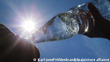 Eine Frau trinkt im Sonnenschein aus einer Perlenflasche sprudelndes Mineralwasser. So gut wie jeder Verbraucher hat die Mehrwegflasche mit der markanten Taille und den 230 charakteristischen Perlen auf der Oberfläche, die an Kohlensäure erinnern sollen, schon in der Hand gehabt. (Zu dpa: «Ein Klassiker: Die Perlenflasche wird 50») +++ dpa-Bildfunk +++