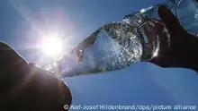 Eine Frau trinkt im Sonnenschein aus einer Perlenflasche sprudelndes Mineralwasser. So gut wie jeder Verbraucher hat die Mehrwegflasche mit der markanten Taille und den 230 charakteristischen Perlen auf der Oberfläche, die an Kohlensäure erinnern sollen, schon in der Hand gehabt. (Zu dpa: «Ein Klassiker: Die Perlenflasche wird 50») +++ dpa-Bildfunk +++
