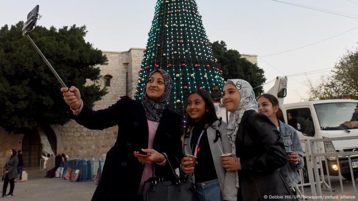 Palestinian girls take a selfie in front of the Christmas tree in Manger Square in Bethlehem