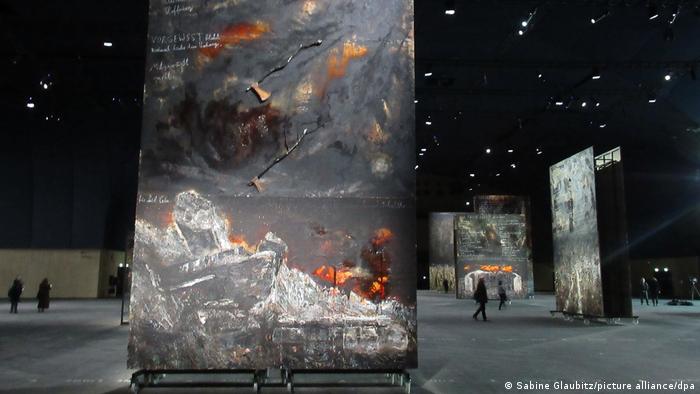 Huge Anselm Kiefer paiting of gray, orange and white in the forefront, with people walking around other paintings in the background.