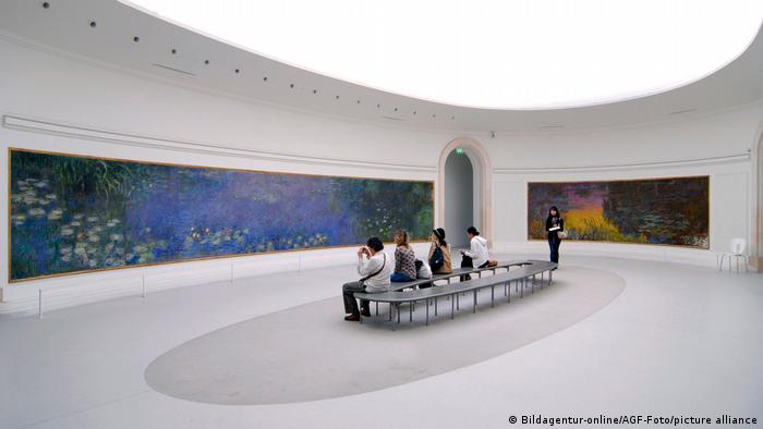 People sitting in a museum looking at a large painting of water lillies, Paris, France 