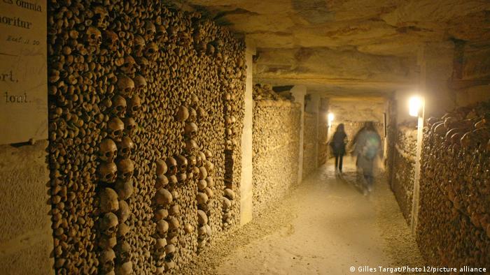 People walking down an underground tunnel with walls of bones in the catacombs, Paris, France