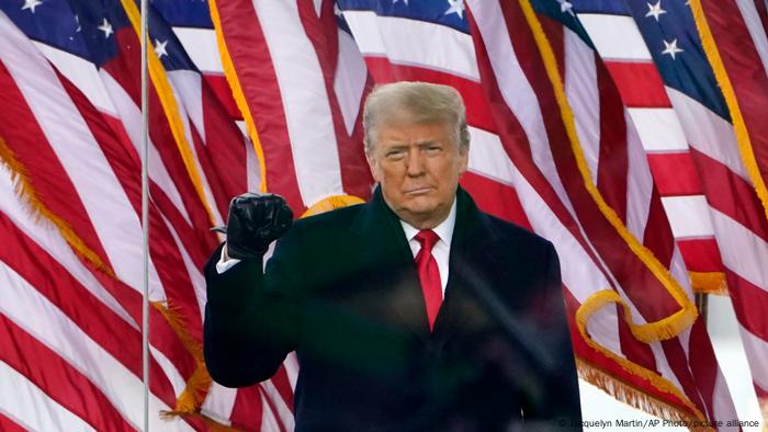 Former US President Donald Trump holds up a closed fist in front of the US flag