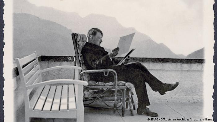 Postkarte: Adolf Hitler in Zivil, auf der Terrasse des Berghofs in einem Korbsessel sitzend und Akten lesend.
