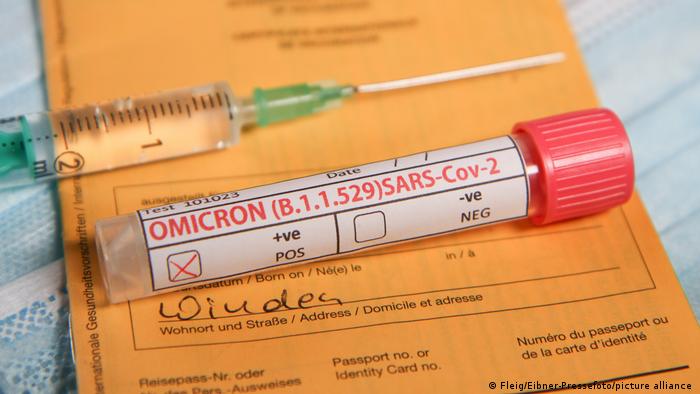 Ein Impfpass mit einer Spritze darauf und ein Teströhrchen, dass besagt: Omikron positiv. 