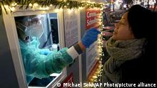 A test center employee performs a coronavirus test as she stands in the 'Kurfuerstendamm (Ku'damm)' shopping road in Berlin, Germany, Tuesday, Dec. 21, 2021. Germany has announced new restrictions aimed at slowing the spread of the new omicron variant of COVID-19. The new rules, which go into effect on Dec. 28, fall short of a full lockdown but include contact restrictions for vaccinated people. (AP Photo/Michael Sohn)