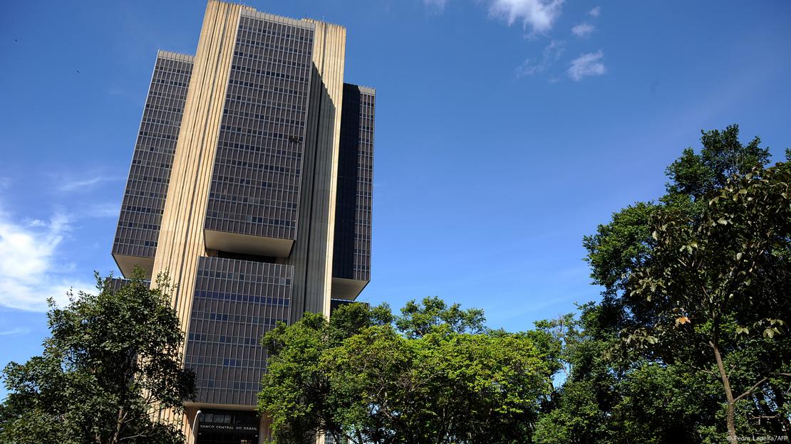 Prédio de arquitetura moderna rodeado de árvores com céu azul ao fundo