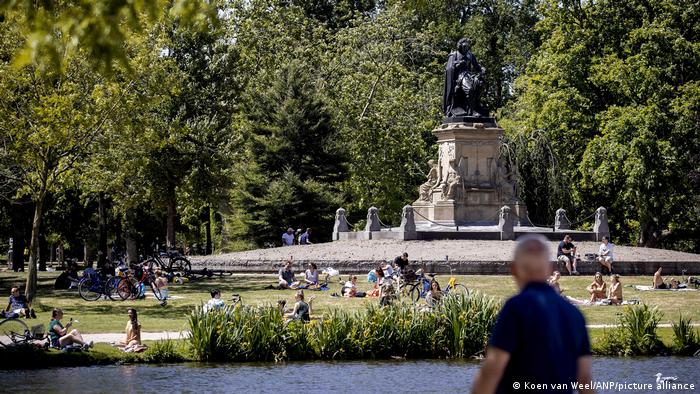 People sit on the grass of the Vondelpark under a statue