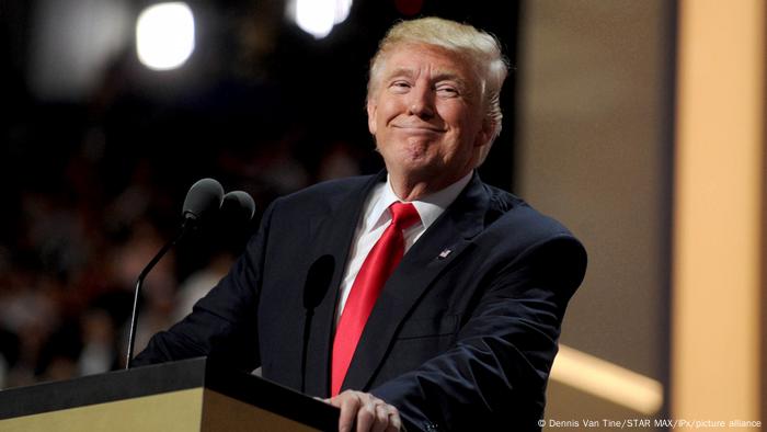 Donald Trump standing at a podium smiling 