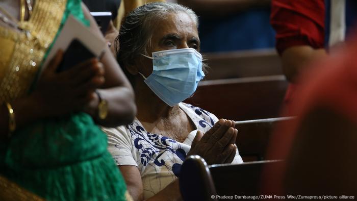 A woman wearing a disposable mask with her hands together in prayer