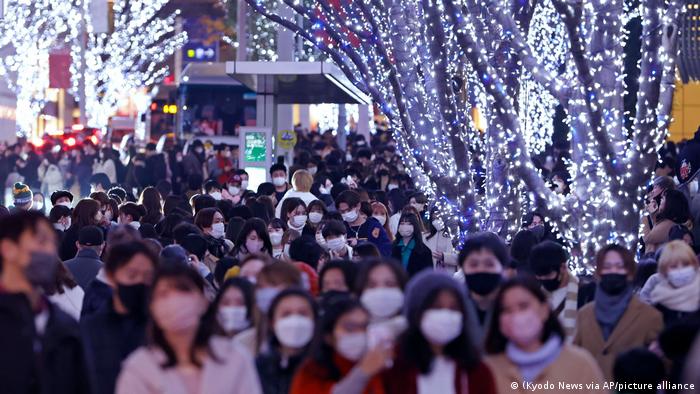 People walk through a crowded Tokyo street illuminated with Christmas lights