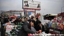 People shop as a billboard displaying the Taliban founder and late supreme leader Mullah Omar (L) and late leader of the Haqqani militant network Jalaluddin Haqqani (R) is seen at a market in Kabul on December 26, 2021. (Photo by Mohd RASFAN / AFP)
