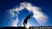 TOPSHOT - A woman throws hot water from a thermos bottle into the cold air making its three phases visible - liquid, gas, solid - as the smallest droplets cool and evaporate in a dramatic cloud before they reach the ground as snow, in Berlin on a sunny but frosty Boxing Day, on December 26, 2021. (Photo by Tobias Schwarz / AFP)