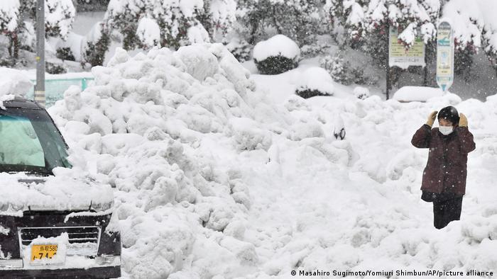 Heavy snow at a street in Tottori City covers a car, as a person is dwarfed by a snowbank