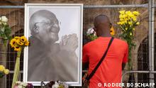 TOPSHOT - A mourner brings flowers to St. Georges Cathedral, where a Wall of Remembrance for South African anti-apartheid icon Archbishop Desmond Tutu has been set up after the news of his death, in Cape Town on December 26, 2021. - South African anti-apartheid icon Desmond Tutu, described as the country's moral compass, died on December 26, 2021, aged 90, President Cyril Ramaphosa said. (Photo by RODGER BOSCH / AFP)