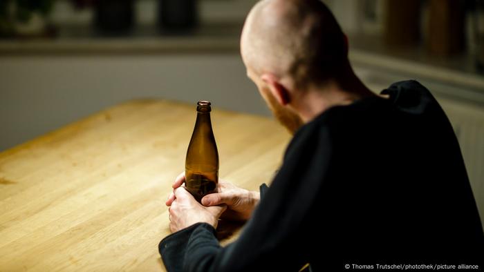 Muškarac sjedi za stolom s bocom piva u rukama