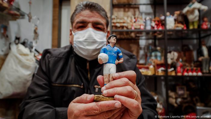  Hugo Maradona holding up a statuette of his brother Diego in a sky-blue Napoli jersey