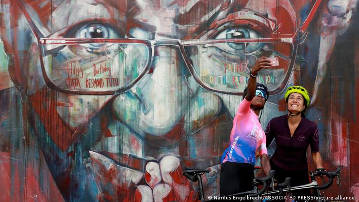 Wandgemälde Desmond Tutus im Street Art-Stil, davor machen zwei Radfahrerinnen ein Selfie
