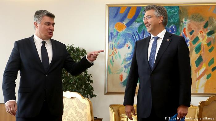 Croatian president Zoran Milanovic pointing at prime minister Andrej Plenkovic, who is standing in front of a colourful painting