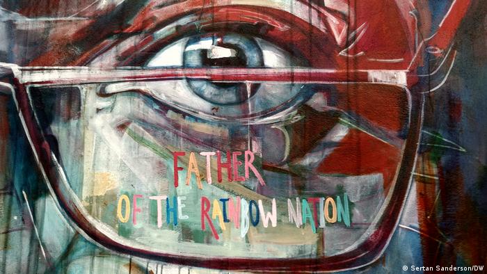 Ausschnitt aus einem Street Art Porträt Desmond Tutus. Zu sehen ist seine Brille und sein linkes Auge, im Brillenglas steht geschrieben: Father of the Rainbow Nation