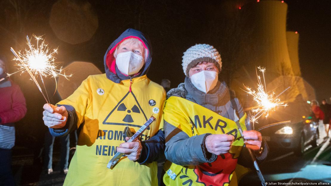 Duas pessoas de camiseta com dizeres antinucleares, segurando fogos de artifício