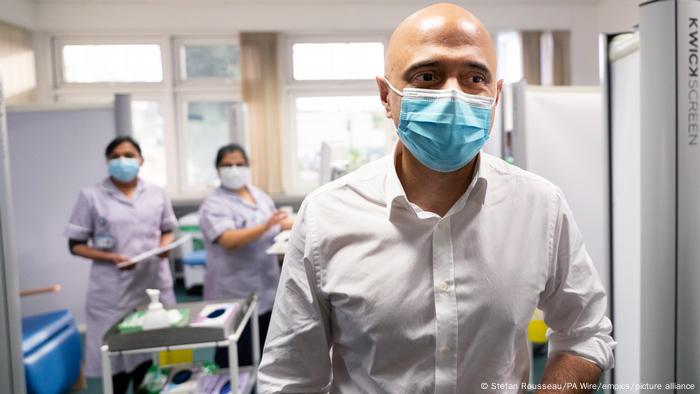 Sajid Javid, hombre con mascarilla, dos mujeres con mascarilla al fondo 