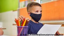 Junge mit Maske wegen Covid-19 als Schüler im Unterricht in der Vorschule oder Grundschule || Modellfreigabe vorhanden