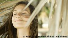 Woman surrounded by dry foliage, eyes closed, hair blowing in wind, close-up || Modellfreigabe vorhanden
