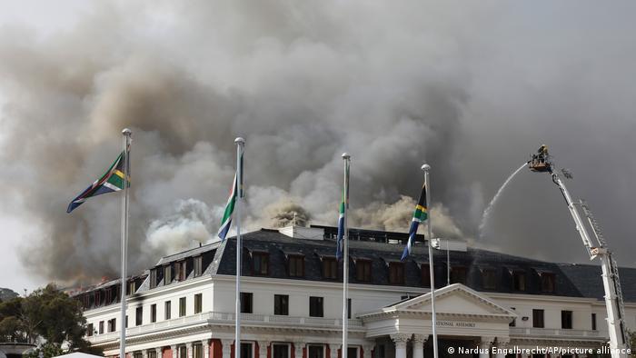 Firefighter on a hoisted platform above South Africa's Parliament spraying water on a new fire at the building