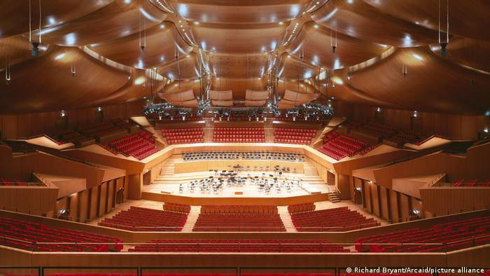 The interior of Sala Santa Cecilia with red seats and suspended wooden ceiling panels. 