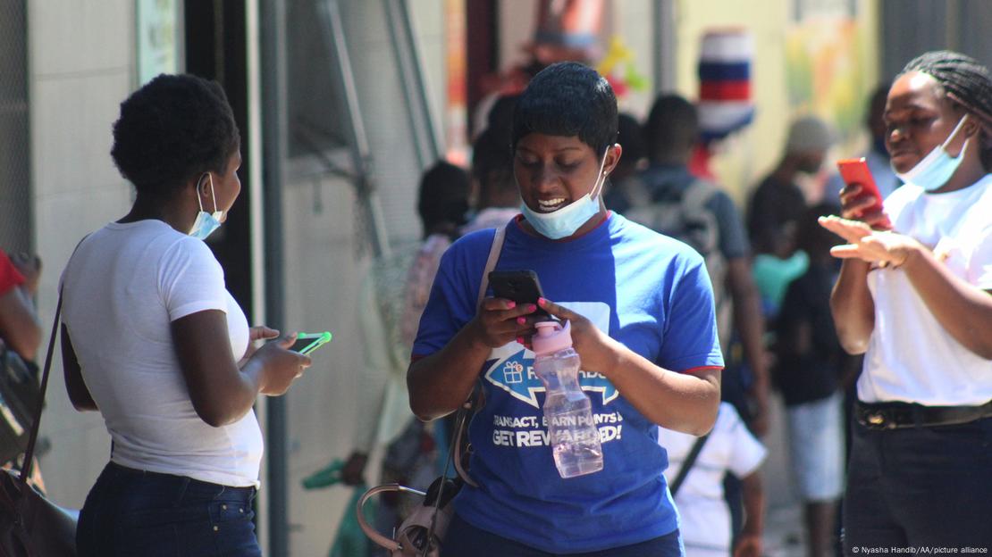 Jovens de máscara no queixo mexem em telefones celulares no Zimbábue