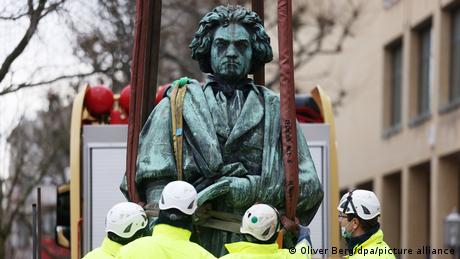 Four people wearing helmets attach harnesses to a statue of Beethoven.