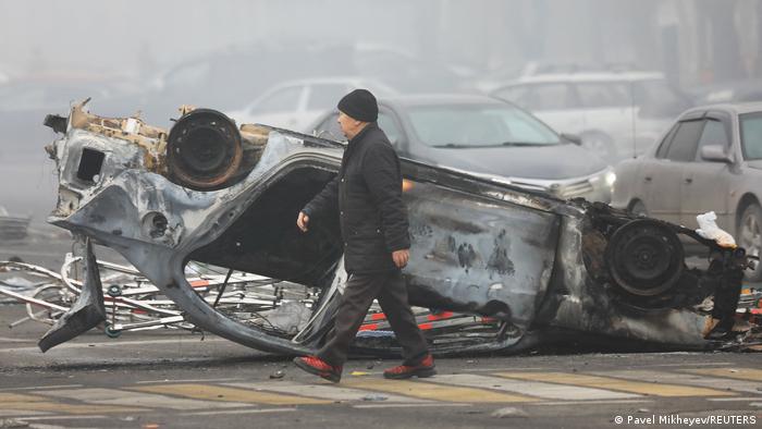 A man walks past a car that was burned during the protests triggered by fuel price increase in Almaty, Kazakhstan