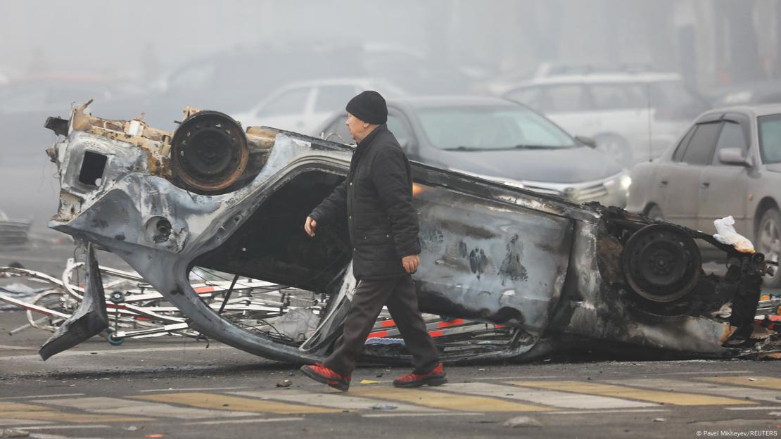 Ein Mann geht an einem ausgebrannten, auf dem Dach liegenden Auto vorbei