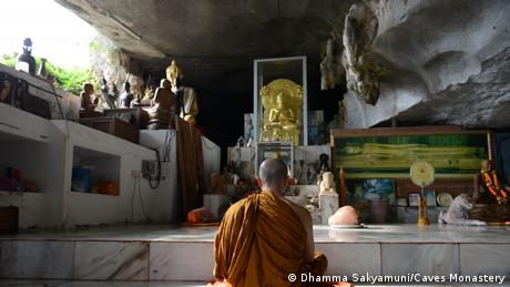 A Buddhist monk sits praying before an alter 