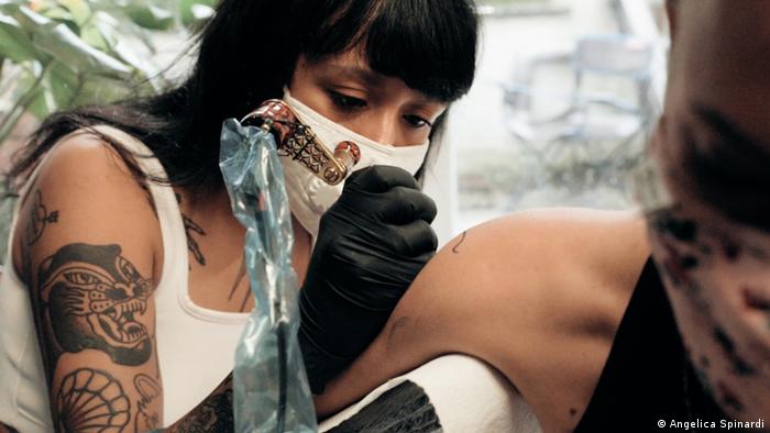 A woman is seen using a tattoo gun to design a tattoo on someone's arm.